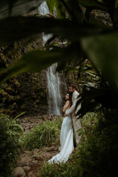 a bride and groom standing in front of a waterfall