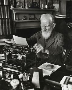 an old black and white photo of a man sitting at a desk with a typewriter