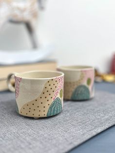 two mugs sitting on top of a table next to each other with designs on them