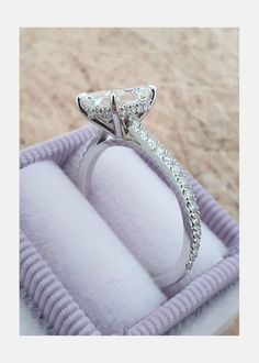 an engagement ring in a box on the beach with sand and water behind it,