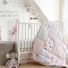 a white crib with pink and gray bedding next to a stuffed animal on the floor