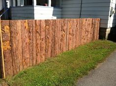 a wooden fence with grass growing on the side of it and a house in the background