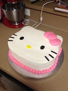 a hello kitty cake with pink icing on a kitchen counter next to a blender