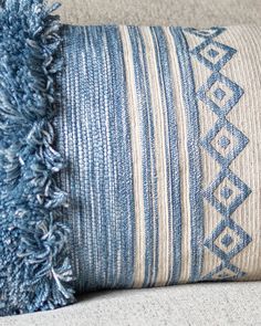 a blue and white striped pillow with fringes on the bottom, sitting on a couch