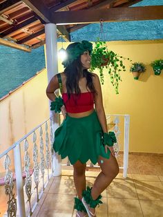 a woman in a green and red outfit standing on a balcony next to a potted plant