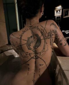 a woman sitting in a bathtub with tattoos on her back