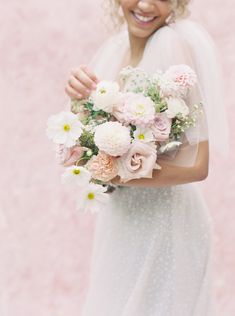 a woman in a white dress holding a bouquet of pink and white flowers on her wedding day