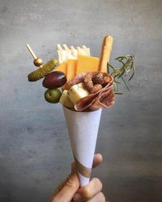 a hand holding up a paper cone filled with different types of cheese and meats