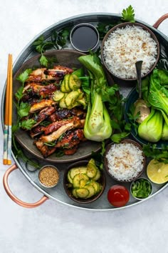 a platter filled with meat, vegetables and rice on top of a white table