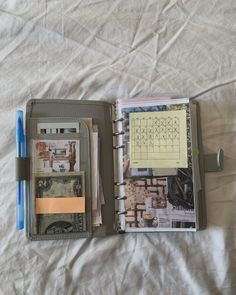 an open planner book sitting on top of a bed next to a pen and paper