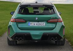 the rear end of a green bmw suv parked on a road in front of a grassy field