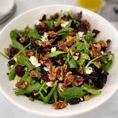 a white bowl filled with green salad topped with cranberries and walnuts on top of a table