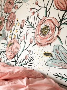 a bed with pink sheets and flowers painted on the wall next to it's headboard