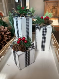 two white boxes with black and white plaid bows are sitting on a table next to pine cones