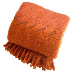 an orange and brown pillow with fringes on the bottom, sitting on a white surface