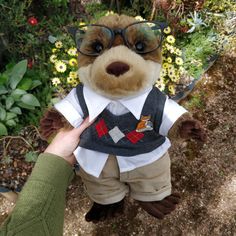 a teddy bear wearing glasses and a shirt with suspenders is being held by a person