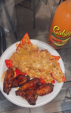 a white plate topped with meat and veggies next to a bottle of orange juice