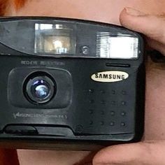 a close up of a person holding a camera in front of their face with one hand