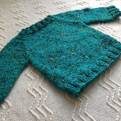 a knitted sweater laying on top of a white tablecloth covered in blue and green speckles