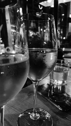 two wine glasses sitting on top of a wooden table next to another glass filled with liquid