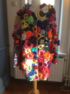 a crocheted jacket is displayed on a stand in front of a window with the sun shining through it