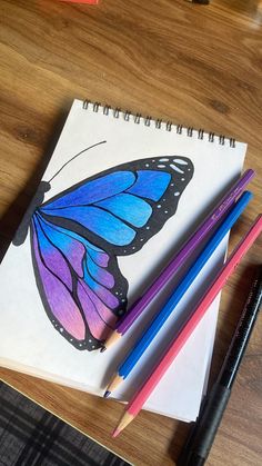 three pencils are sitting on top of a notebook with a butterfly drawn on it