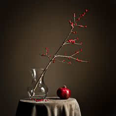 an apple sits on a table next to a vase with red berries and a twig