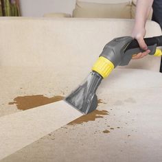 a person is using a vacuum to clean a couch with brown stains on the floor