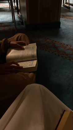 a person sitting on the floor reading a book with their hands resting on an open book