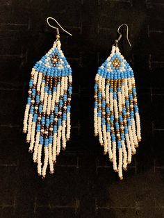 two pairs of beaded earrings are shown on a black surface, one is blue and the other is white