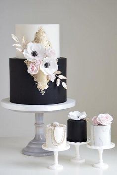 a black and white cake with pink flowers on the top is surrounded by other cakes