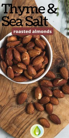 roasted almonds in a white bowl on a wooden cutting board with thyme and sea salt