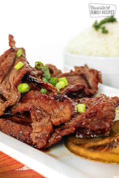 a white plate topped with meat and veggies next to a bowl of rice