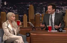 a woman sitting next to a man on top of a table with cups in front of her