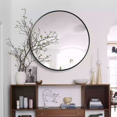 a mirror on the wall above a shelf with vases and plants in it,