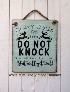 a sign hanging on the side of a white wooden wall that says, crazy dogs live here don't knock they will bark i will tell you shall steal it