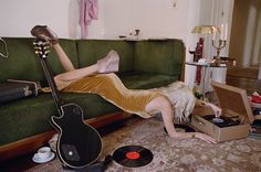 a woman laying on top of a green couch next to a guitar and record player