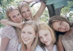 a group of young women standing next to each other in front of a leafy tree