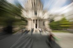 blurry photograph of people walking in front of a building with trees on the side