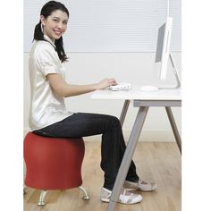 a woman sitting at a desk with a computer on top of her lap and smiling