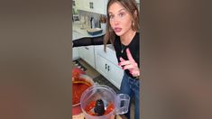 a woman standing in front of a blender filled with red liquid and pointing at the camera