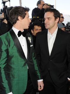 two men in tuxedos standing next to each other with cameras around their backs