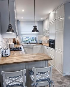 a kitchen with white cabinets and wooden counter tops next to two chairs at the island