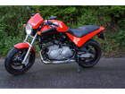 an orange and black motorcycle parked on the side of the road in front of some bushes