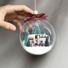 a hand holding a christmas ornament with a house in it