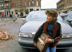 a young boy holding a briefcase standing in front of a car on a city street