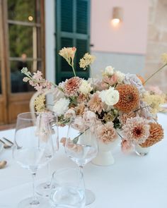 an arrangement of flowers in vases on a table with wine glasses and utensils