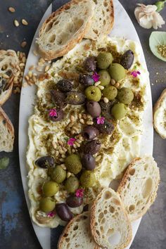 an assortment of breads and olives on a white platter next to other food