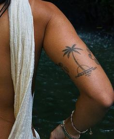 a woman with a palm tree tattoo on her upper arm and lower arm is standing in the water