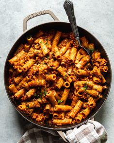 a skillet filled with pasta and sauce on top of a table next to a towel